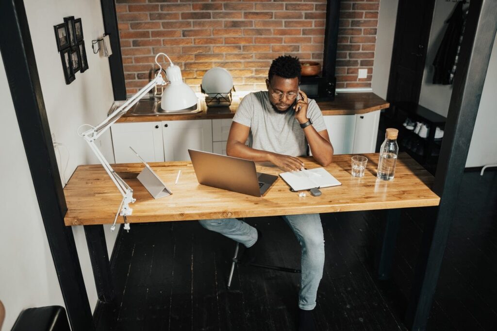 Man running his Screenmobile franchise from home at a wooden desk. He sitting at the desk on the phone and writing notes on a paper.